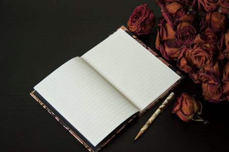 Red dry rose flowers and notebook. Romantic vintage composition on dark background.