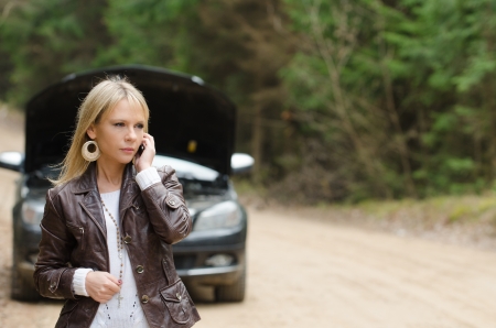 Young woman at broken car with mobile phoneの写真素材