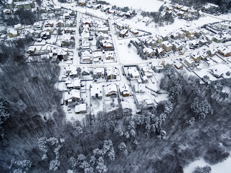 Aerial top view of snowy forest and detached houses in winterの写真素材
