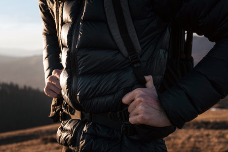 Close-up of a hiker tightening the straps on their backpack during a hike. The scene captures the...