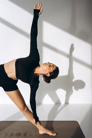 Woman in Triangle Pose During Yoga Session with Sunlit Shadowsの写真素材