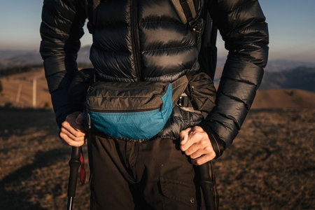 A detailed close-up of a hiker's gear, focusing on the waist pack and trekking poles, against the...
