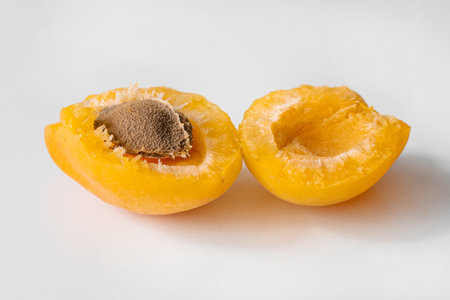 A close-up photograph of a halved apricot displaying its seed and vibrant, juicy interior. The detailed texture of the fruit's flesh and seed is captured beautifully, emphasizing the freshness and ripeness of the apricot. This image is perfect for use in food photography, health blogs, or as an illustration in nutritional articles.の写真素材