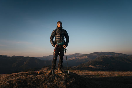 A solo hiker stands on a mountain peak at sunrise, equipped with trekking poles and a backpack, enjoying the expansive view of the mountain range.の写真素材