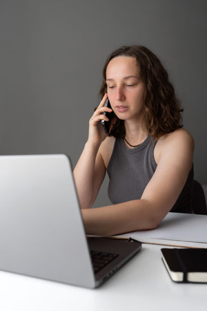Woman managing work calls while sitting at home with laptop and notebook