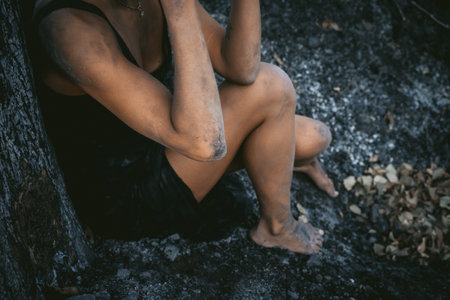 Woman sitting against a burnt tree, reflecting on forest fire impact and resilienceの写真素材