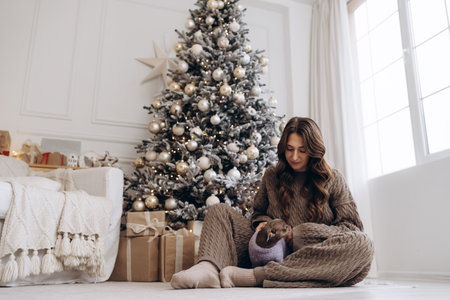Woman in cozy knitted outfit sitting with a Chihuahua near a decorated Christmas treeの写真素材