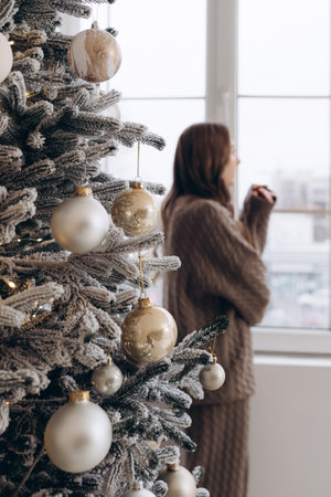 Woman looking out the window near a decorated Christmas treeの写真素材
