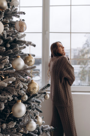 Woman looking out the window near a decorated Christmas treeの写真素材