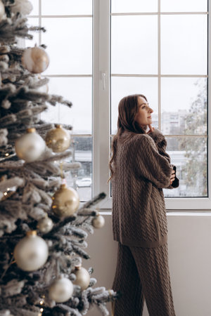 Woman looking out the window near a decorated Christmas treeの写真素材
