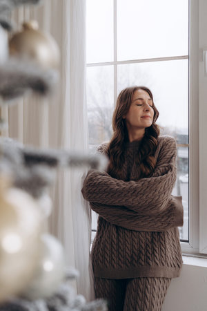 Woman looking out the window near a decorated Christmas treeの写真素材