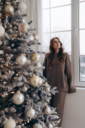 Woman looking out the window near a decorated Christmas treeの写真素材