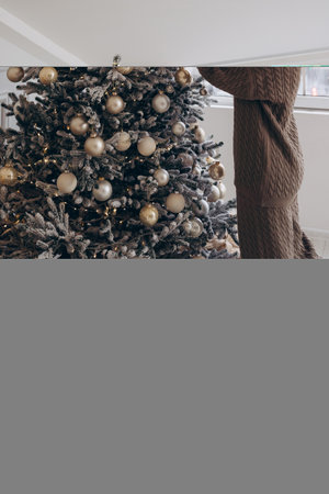 Woman decorating a Christmas tree with golden ornamentsの写真素材
