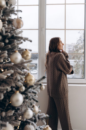 Woman looking out the window near a decorated Christmas treeの写真素材