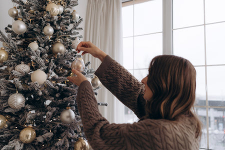 Woman decorating a Christmas tree with golden ornamentsの写真素材