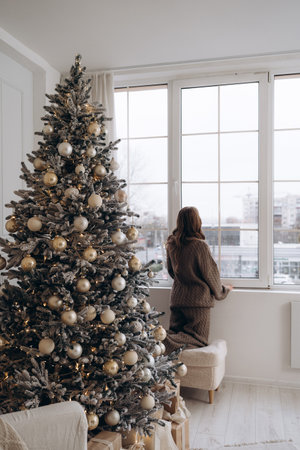 Woman looking out the window near a decorated Christmas treeの写真素材