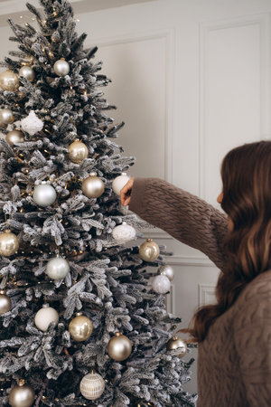 Woman decorating a Christmas tree with golden ornaments