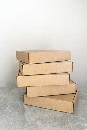 A stack of self-assembly kraft cardboard boxes arranged on a textured surface. Ideal for packaging, gift wrapping, and shipping. A sustainable choice for businesses and holiday preparations.の写真素材