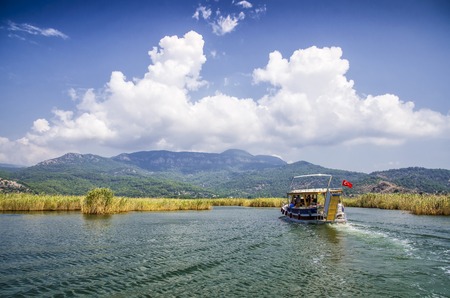Pleasure boat with tourists in the mouth of the Dalyan River under Lycian tombsのeditorial素材