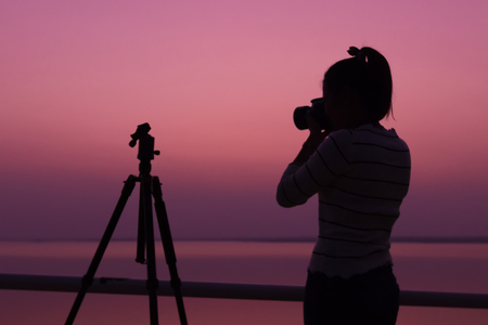 Silhouette woman photographer shooting sunset,Silhouette photographer with sunsetの写真素材