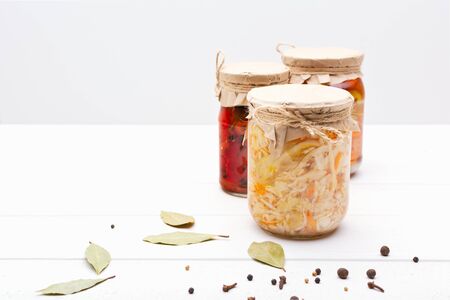 Pickled fermented cultivated cabbage, tomatoes, peppers, carrots, assorted, mix in a glass jar for canning on white wooden table, bay leaf, black pepper, coriander seeds. stand right angle. horizontal.の写真素材