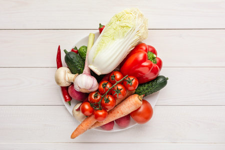 Various raw vegetables on a white plate and wooden background with blank space around. Zucchini, cucumber, chili pepper, mushrooms, tomatoes, cauliflower, lettuce, carrots.の写真素材