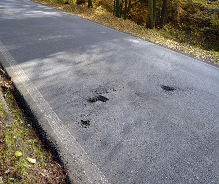 Damaged asphalt pavement road with potholes caused by freeze and thaw cycle during winter の写真素材