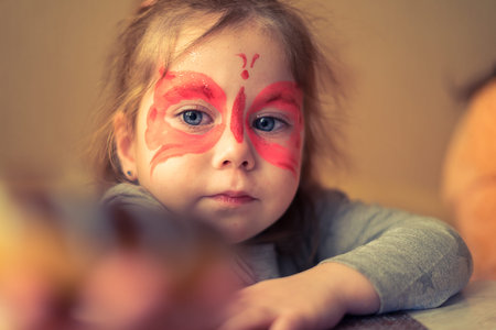 Little girl with a painted mask on her face in the form of pink butterfliesの写真素材