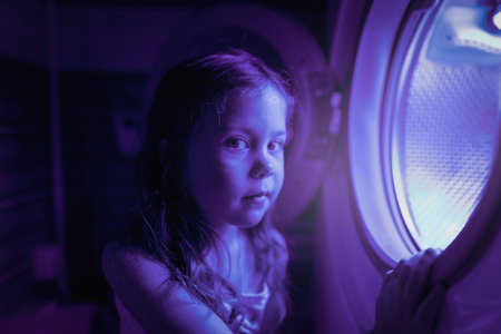 Little girl plays with the washing machine as if it were a spaceship