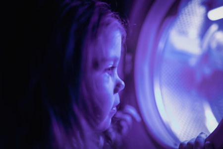 Little girl plays with the washing machine as if it were a spaceship