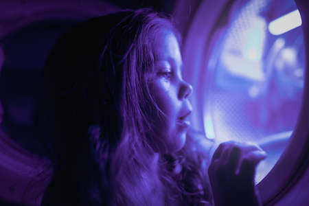 Little girl plays with the washing machine as if it were a spaceshipの写真素材