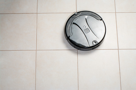 white Robot vacuum cleaner cleaning dust on tile floors in kitchen. Modern smart cleaning technology housekeeping. Space for text. top view.の写真素材