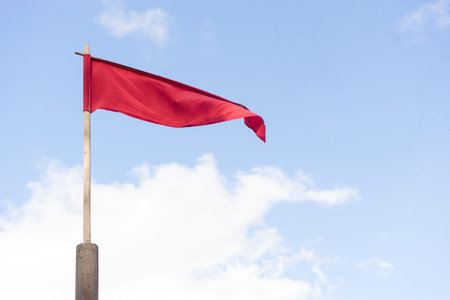 narrow red swinging flag on wooden flagpole against sky.