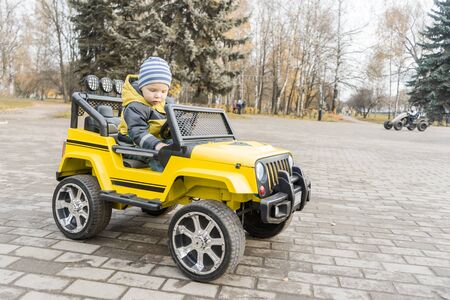 toddler with enthusiasm study control of yellow children car with an electric motor in autumn city Park.の写真素材