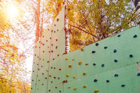Artificial climbing wall with hooks for kids and adults in natural amusement Park on sunny day. Concept of healthy lifestyle, fitness, extreme sports, development of endurance.の写真素材