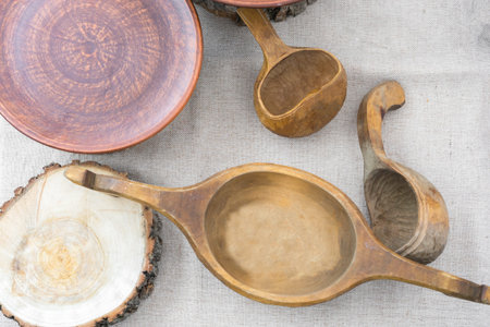 vintage traditional wooden utensils: a vessel for drinks and spoons, a clay ceramic plate, a cut of...