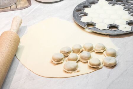 Process of making homemade dumplings with meat. Rolling out dough with wooden rolling pin. Form for modeling with filled cells. The finished product is in center.の写真素材