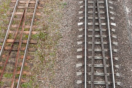 Two parallel railway tracks. top view. On left is old rusty road with wooden sleepers. On right is new shiny one with reinforced concrete support for rails.の写真素材
