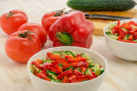 Vitamin salad of ripe tomatoes, fresh, green cucumbers and red bell peppers in glass white bowl on light wooden table. Ingredients. Vegetables. Healthy lifestyle. Products for diet and weight loss.の写真素材