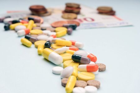 Path of tablets of different sizes and colored capsules leads to paper banknotes and coins. Concept of high profitability from production and sale of medicines, vitamins, and dietary supplements.の写真素材