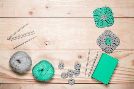 Knitting accessories. Balls of yarn. Crocheted gray-green square-shaped napkins. Plastic grey hooks on light wooden background. Copy Space. close-up, top view. Place for text.の写真素材