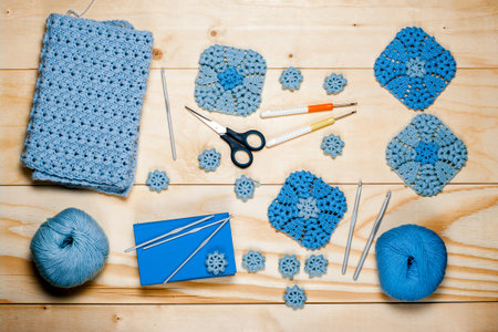 Composition of knitting accessories. Blue crocheted square-shaped napkins, balls of wool yarn, scissors, crochet hooks on wooden background. view from the top, flat layer.の写真素材