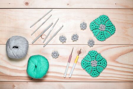 On light wooden background composition of knitting tools, gray-green balls of yarn and crocheted napkins for your design, template, postcard, decoration. Hobbies in free time.の写真素材