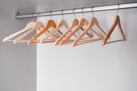 Many empty hangers made of natural, light wood of different shades hang on metal rod in wardrobe. High-quality accessories in modern furniture.の写真素材