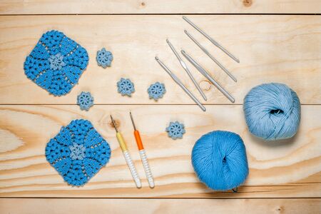 On light wooden background composition of knitting accessories, blue balls of yarn and crocheted napkins close-up top view for your design, template, postcard, decoration. Hobbies in free time.の写真素材