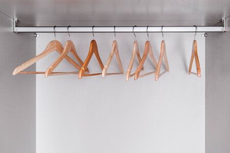 Many empty, lacquered light wood clothes hangers hang in wardrobe on metal rod. Internal space of furniture.の写真素材