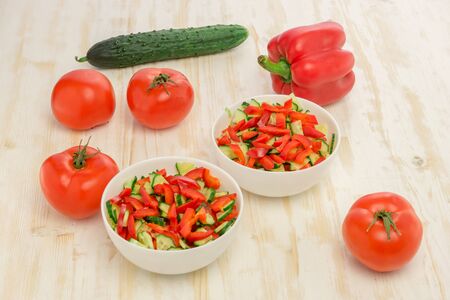 Fresh salad of sliced green cucumbers, red tomatoes and bell peppers on wood table. Vegetables. Gluten-free, lactose-free vegan food.の写真素材