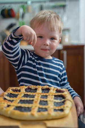 Little cute blond boy sweet tooth is looking forward to trying berry pie with jam.の写真素材