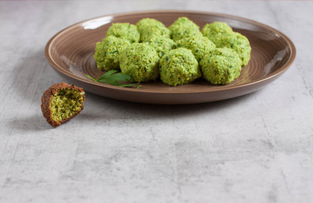 Raw uncooked falafel balls on a plate ready to be cooked next to a ready falafel ball with a bite. Cooking at home/healthy cooking concept. Selective focus, copy space. Concrete background.の写真素材