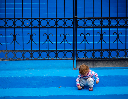 Little girl playing with herself on bright blue stairs with fenceの写真素材